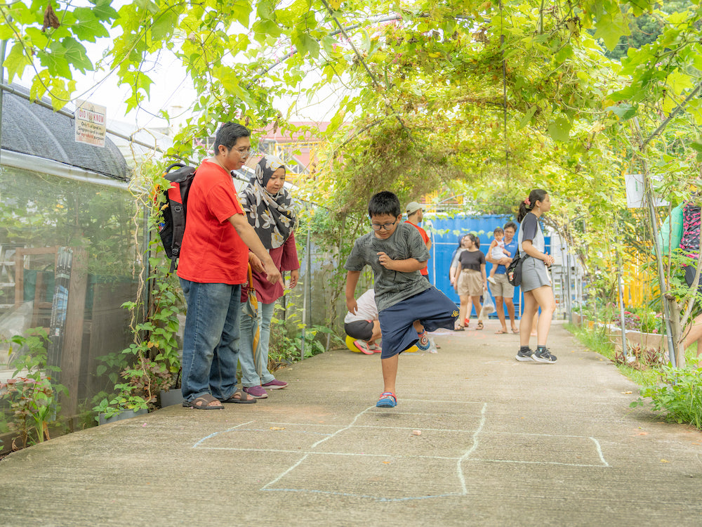 A young boy playing hopscotch under the City Sprouts trellis.