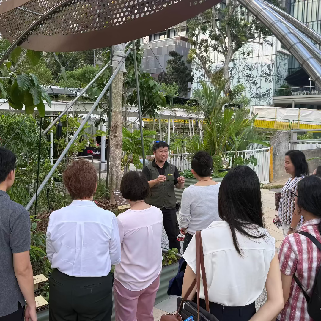 Group of people gathered around a modern architectural structure with greenery in the background.